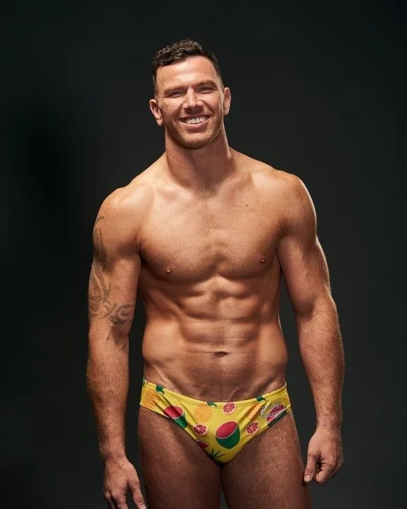 Sorrindo rapaz musculoso em cuecas de nado amarelo frutado flexionando abdominais para a câmera