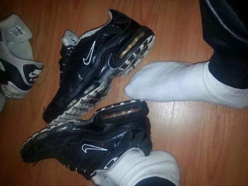 Cara de meias brancas brincando com Nike Air Max, pés na frente e centro no chão de madeira