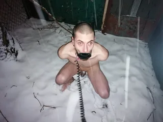Cara pervertido ajoelhado nu na neve com telefone receptor mordaça e bola de metal mordaça, intenso contato visual