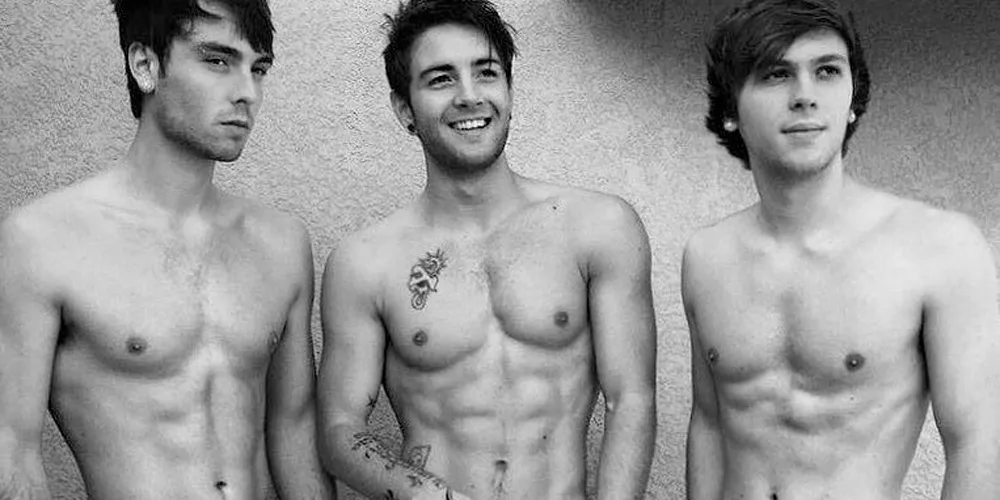 Emblem3 shirtless trio smirking in moody black and white studio