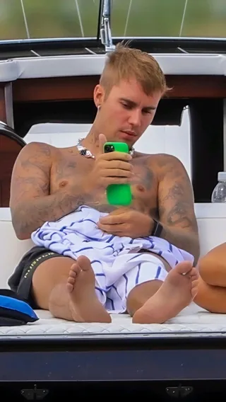 Justin Bieber sem camisa em um iate rolando seu telefone