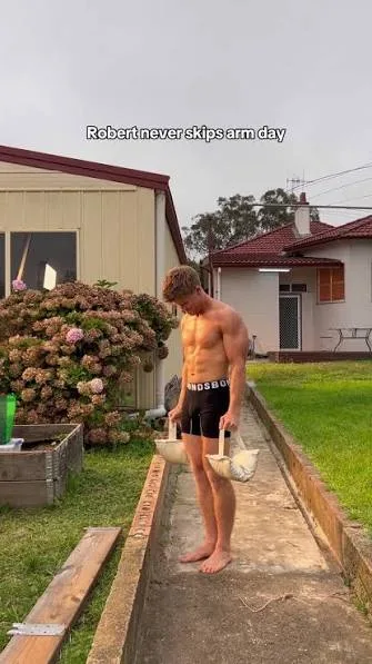 Robert Irwin snørefri i sorte shorts bærer tasker ned ad en havesti