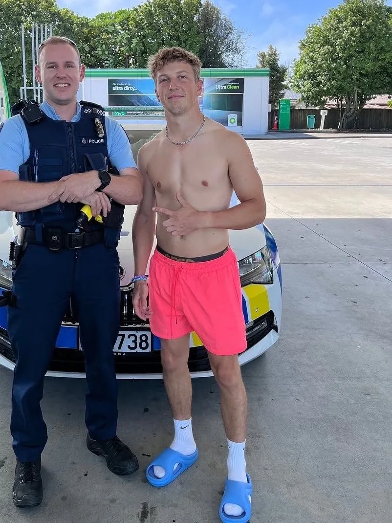 Skjoldløs dreng i varme lyserøde shorts og blå dias udgør bare- chested ved siden af betjent bil
