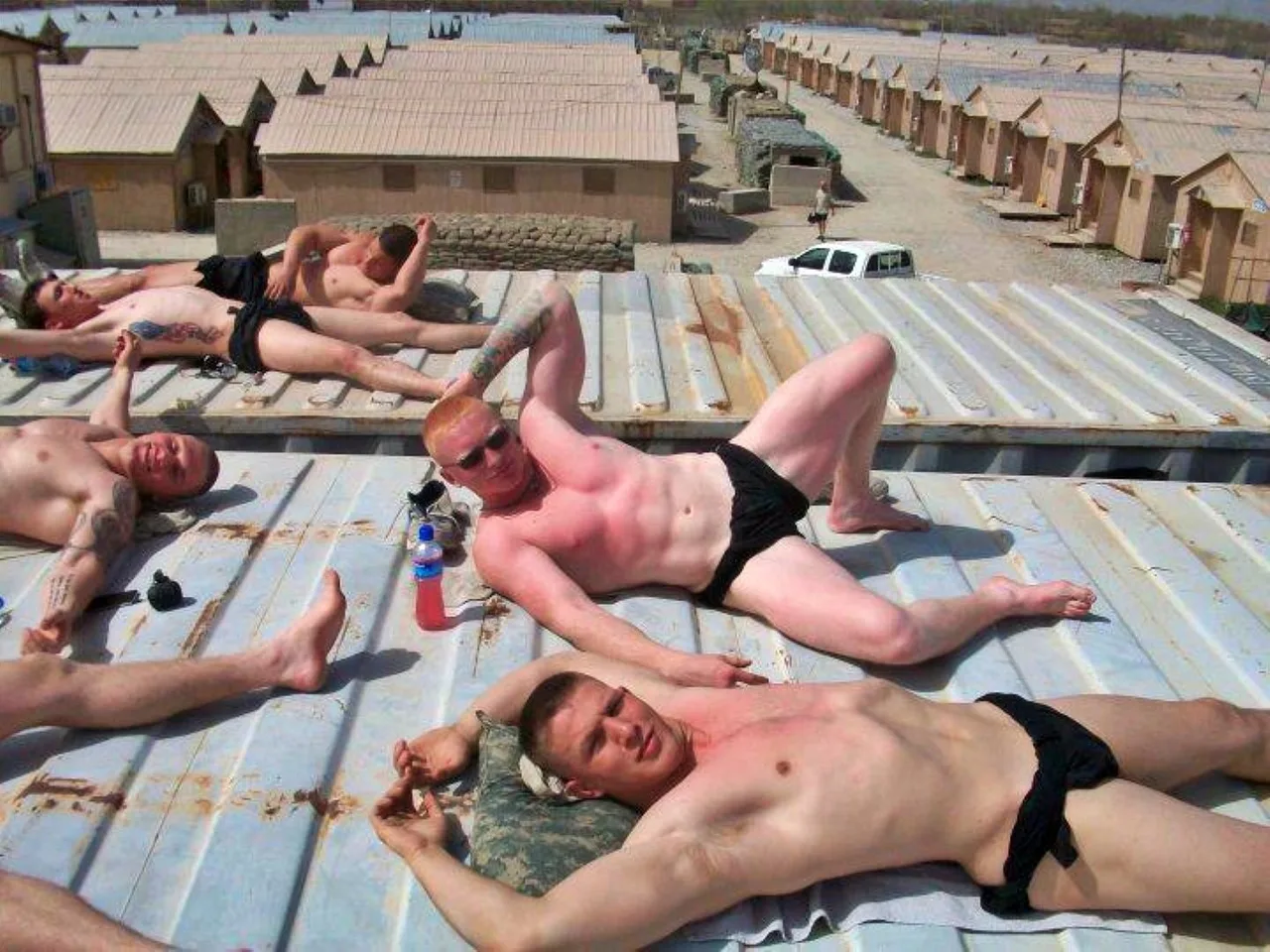 Caras de estilo militar, com calções pretos, espalham-se em telhados de metal quente, brilhando pela pele, abdominais em exposição