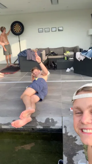 Lazy lang poolside com os pés descalços, sem camisa e sorrindo para a câmera