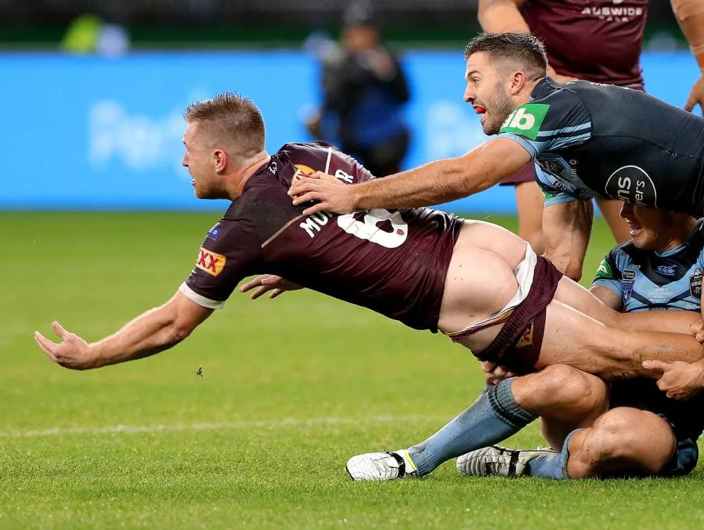 Hård rugby dreng i maroon kit bliver tacklet midt-dyk, røv kind udsat, bolde skjult under shorts