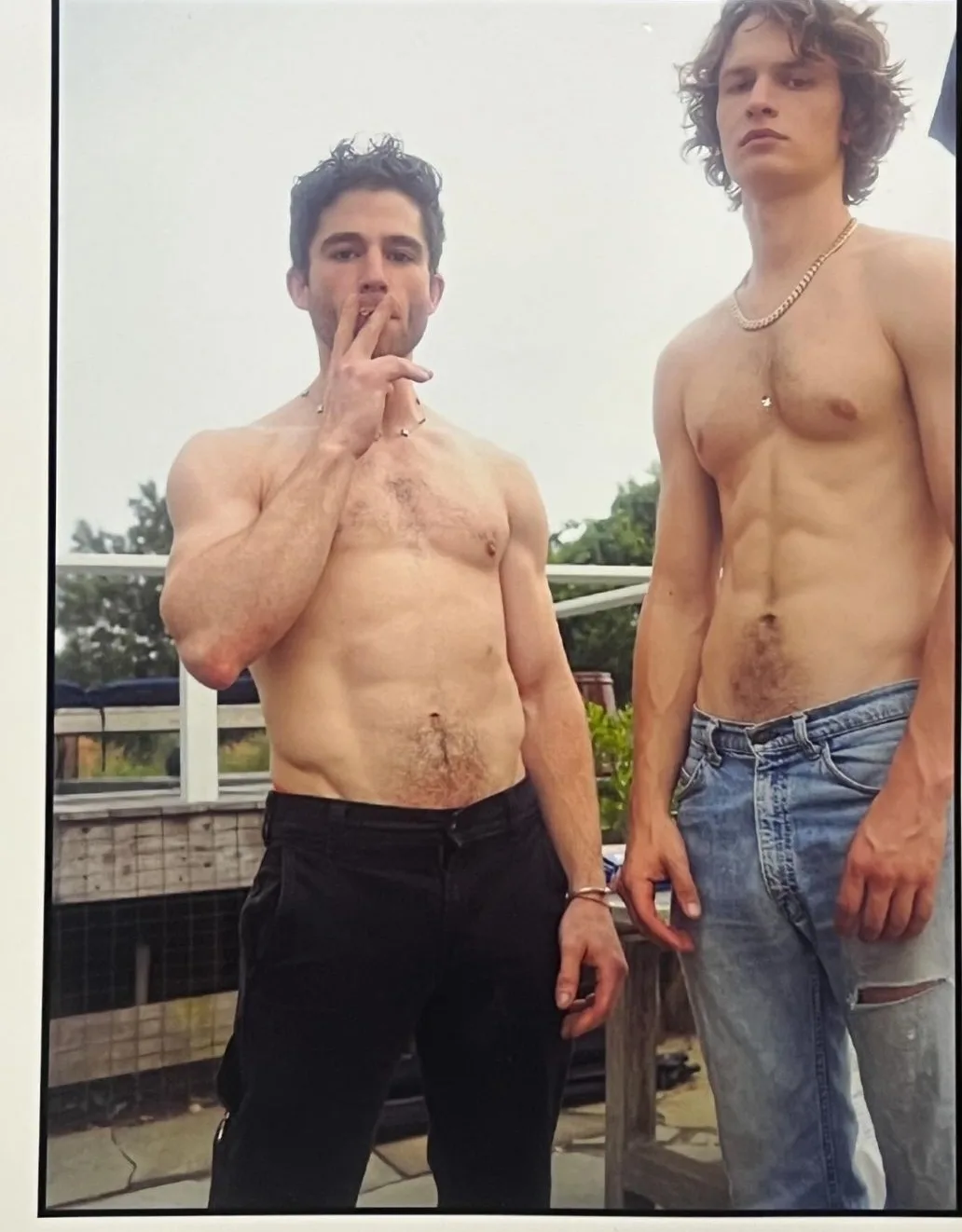 Ansel Elgort shirtless med mejslet abs og brysthår, poserer ved siden af en anden bare- chested fyr i rippede jeans