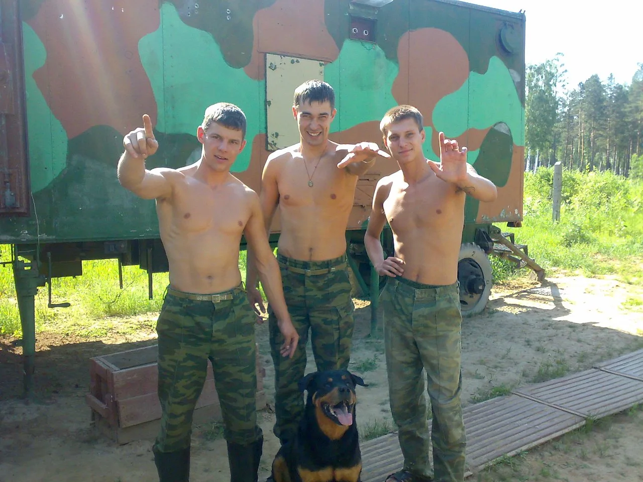 Tre skjoldløse slavisk hær fyre i camo bukser poserer bare- chested med en rottweiler af en militær lastbil