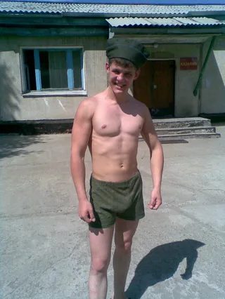Rapaz de estilo militar sem camisa de shorts verdes e sorrisos de boné ao ar livre