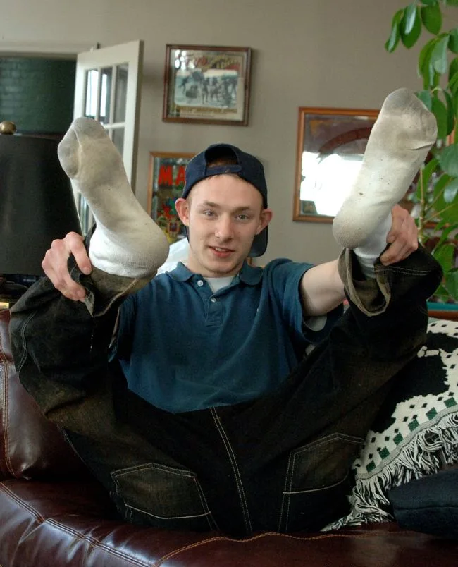 En fyr i beskidte sokker bøjer såler mens han ligger på sofaen, jeans ned til lårene