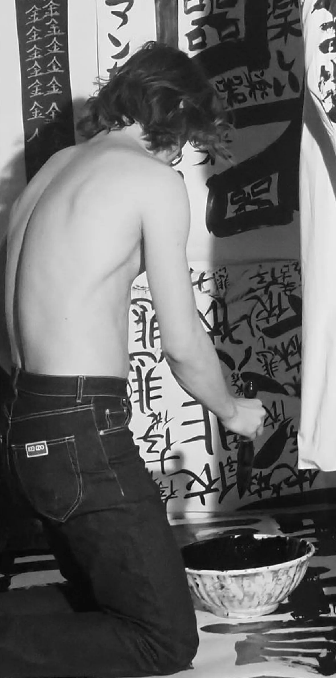Ansel Shirtless Elgort arrodilla la espalda, músculos esculpidos en exhibición contra el arte de la caligrafía audaz