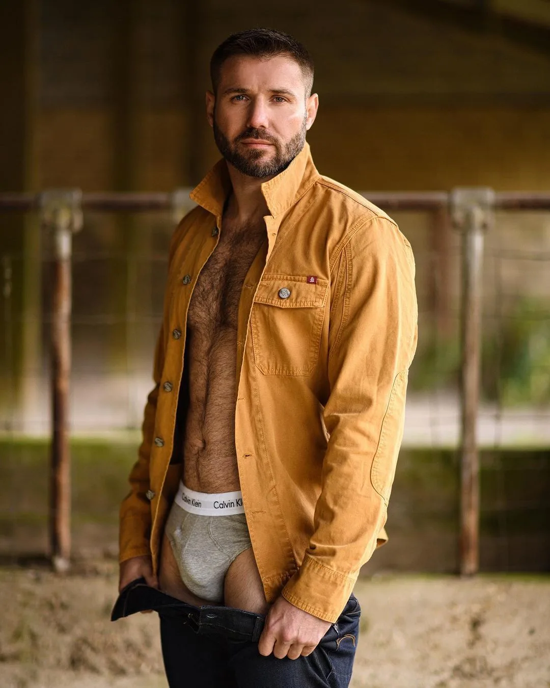 Bärtiger Stutzen in offenem Arbeitshemd blinkt graue Calvin Klein Slips, während er Jeans ausreißt