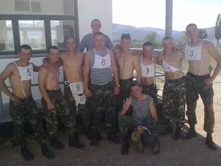 Caras de estilo militar com calças de camuflagem e coletes listrados posando sem camisa ao ar livre