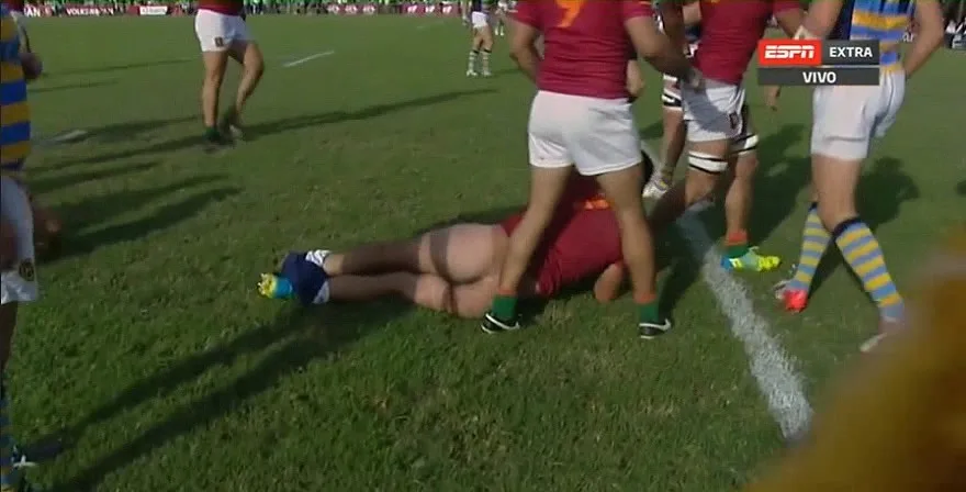 Sexy rugby lad sprawled on grass with tight shorts riding up, mates standing close