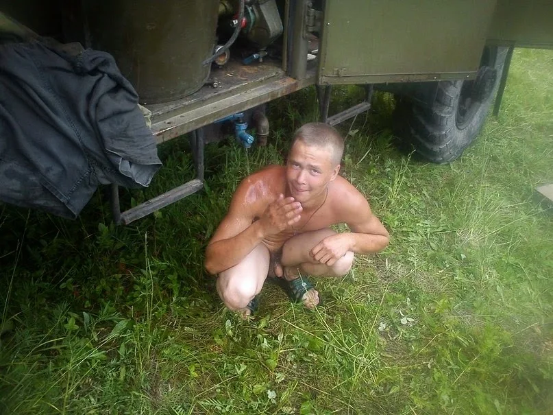 Shirtless military-style lad squatting barefoot in grass beside truck, all natural and sweaty