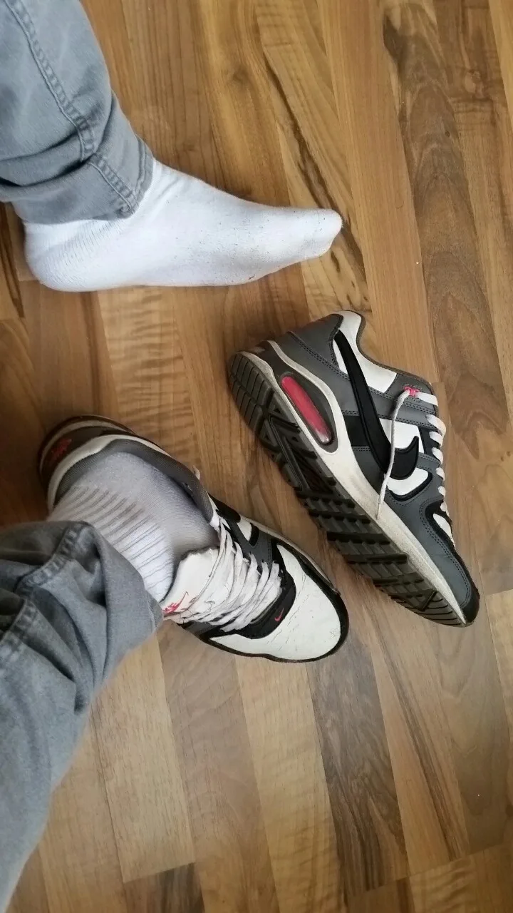 Fyren i grå jeans og sokker sparker sneaker af, foden flettet på trægulv