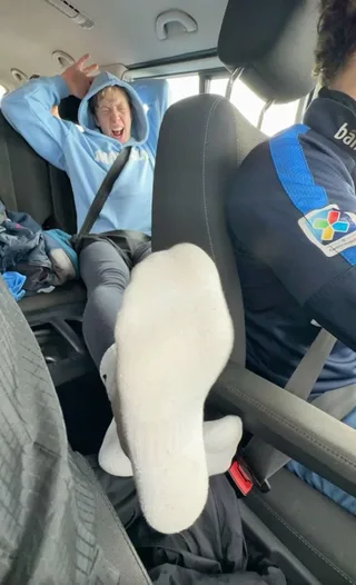 Rapaz preguiçoso de capuz chuta de volta com os pés descalços no carro, boca aberta no meio do grito