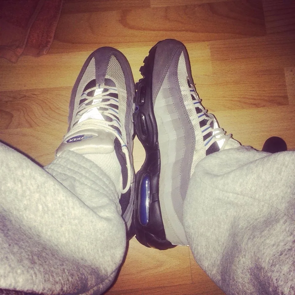 Lazy dreng i grå sweats og Nike Air Max 95s, fødder skruet på trægulv