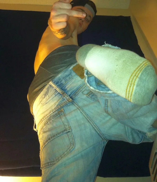 Um cara com calça jeans rasgada pisca sola meia enquanto flexiona a bunda e dá o dedo médio