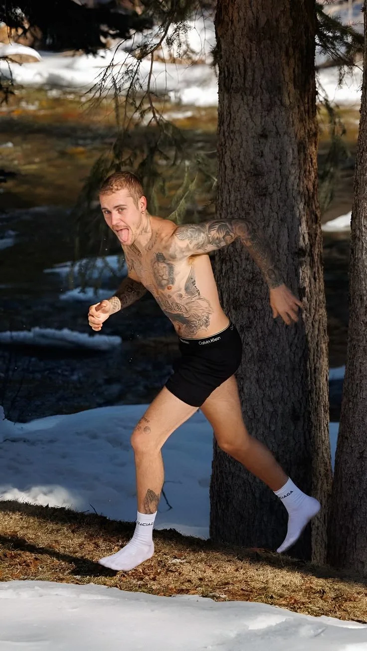 Skjult Justin Bieber i sorte bokserunderbukser og hvide sokker legende mod et træ i sneagtige skove