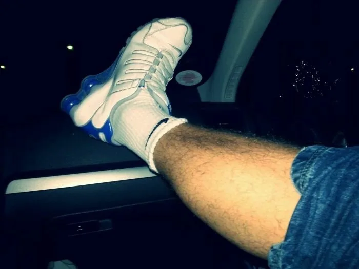 Hairy ben i denim shorts proppet op med hvid sneaker og sok, bil interiør vibe