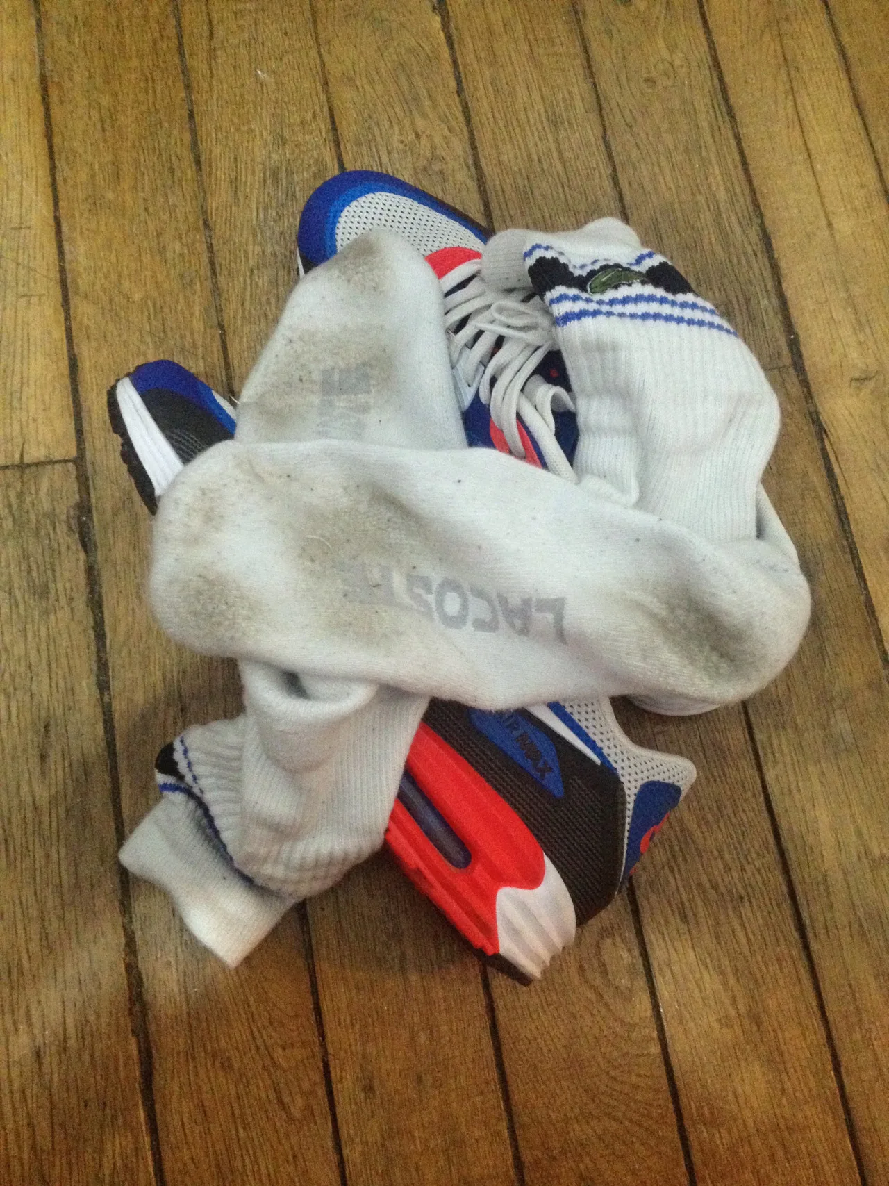 Dirty Lacoste sokker tanglet med farverige sneakers på et trægulv