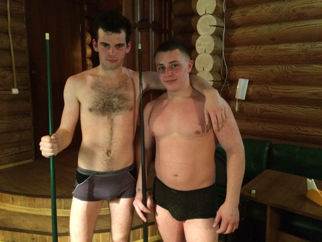 Dois caras em pose de boxers confortáveis com tacos de bilhar em uma cabana de madeira rústica