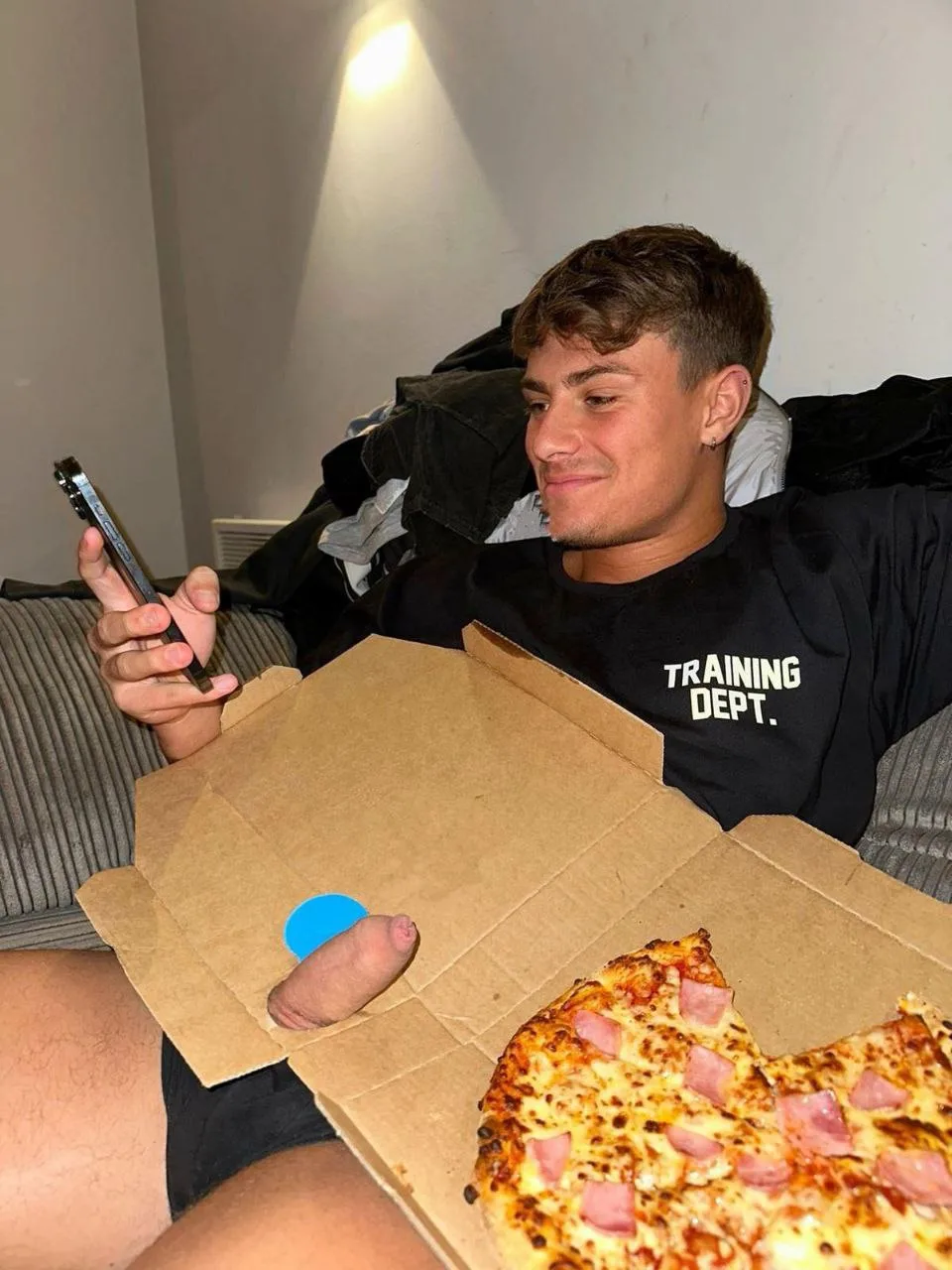 Rapaz preguiçoso sorrindo para o telefone com caixa de pizza escondendo seu pau duro