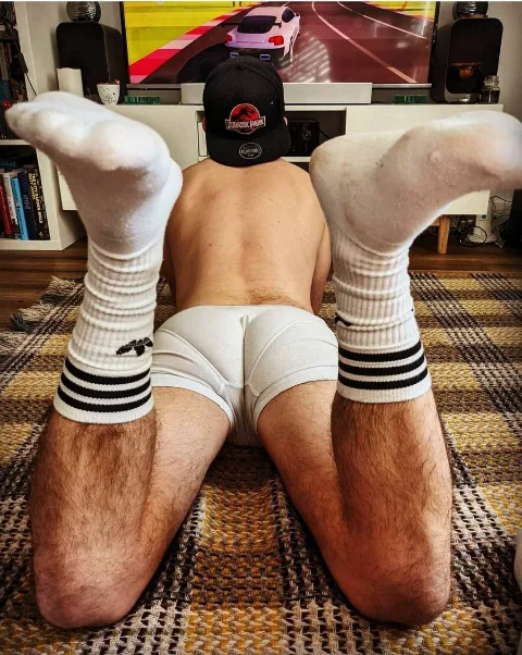 Guy in white briefs and striped socks kicks back gaming, feet up, ass on display