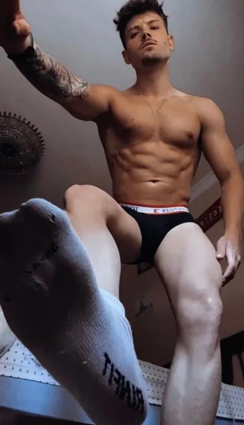 Muscular lad in briefs flexes abs while showcasing socked feet up close for foot fetish fans