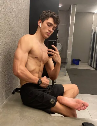Muscle lad takes mirror selfie showing bare feet and ripped abs in gym locker room