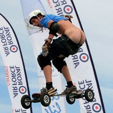 Skateboarding lad in blue tee and low shorts shows off his ass mid-air trick