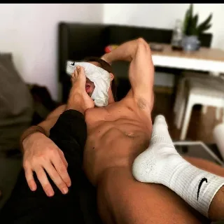 Muscular guy in white socks teasing with feet over his face, shirtless and relaxed on couch