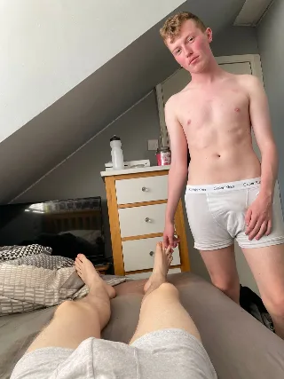 Blond lad in white boxers teasing with bare feet while standing over a guy on bed