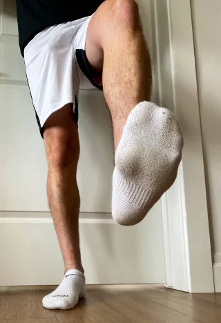Guy in white shorts lifts socked foot, showing sole and hairy legs up close