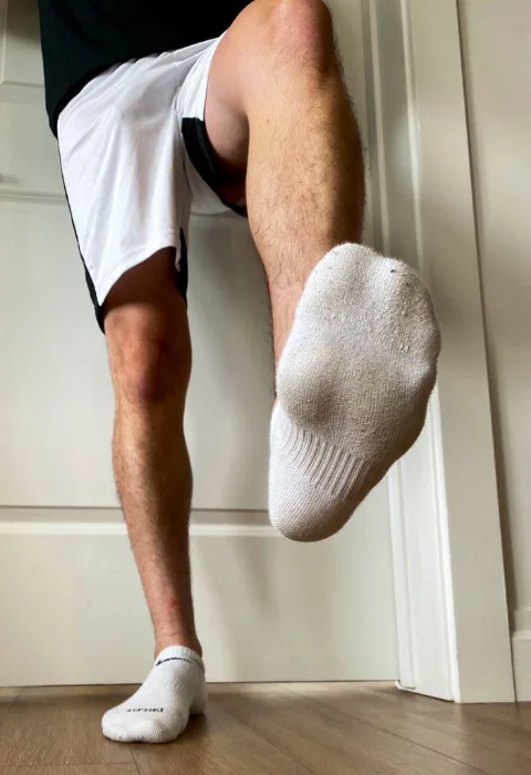 Guy in white shorts lifts socked foot, showing sole and hairy legs up close