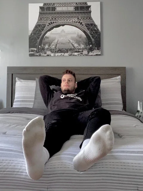 Lazy lad in socks sprawled on bed, feet up, Eiffel Tower art behind