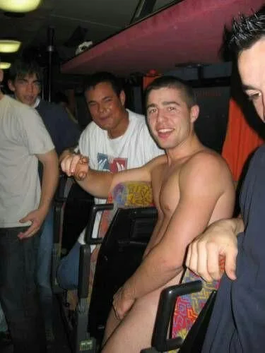 Garoto sorridente sem camisa exibindo o peito e os abdominais em um ônibus de festa lotado
