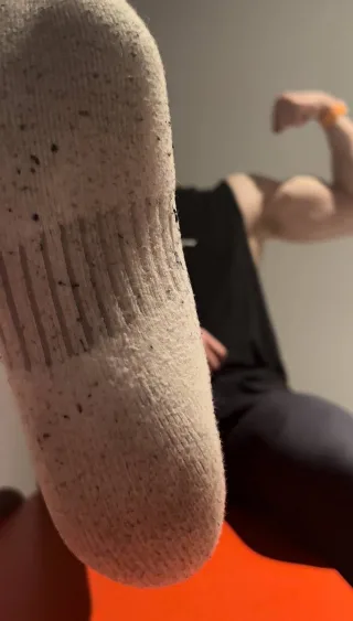 Muscular lad flexing bicep while showcasing speckled sock sole up close