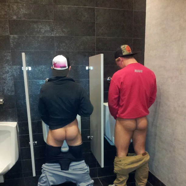 Two lads caught mid-piss in a public restroom, pants down, bare ass on display