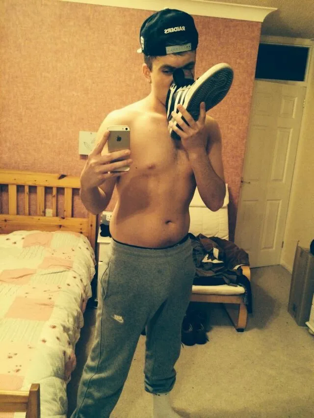 Shirtloze schunnige jongen in grijs zweet neemt spiegel selfie terwijl snuffelen zijn sneaker