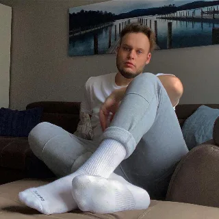Lazy lad in white socks and grey sweats lounging on couch with feet front and center