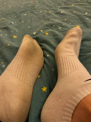Dirty athletic socks on bare feet resting on starry sheets, foot fetish tease