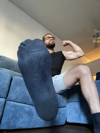 Bearded muscle guy flexing bicep with socked foot kicked up close to camera