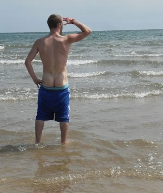 Beach lad in blue trunks showing off his bare ass while shielding eyes from sun