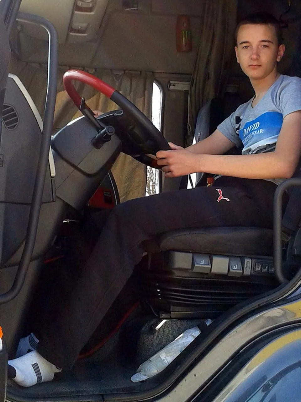 Truck driver dreng i Puma joggere & hvide sokker greb hjul, fødder synlige under bindestreg