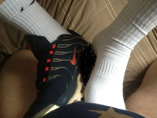 Facet w białych skarpetach i Nike dekolt zginanie stóp na łóżku, kogut zamazany, ale widoczny