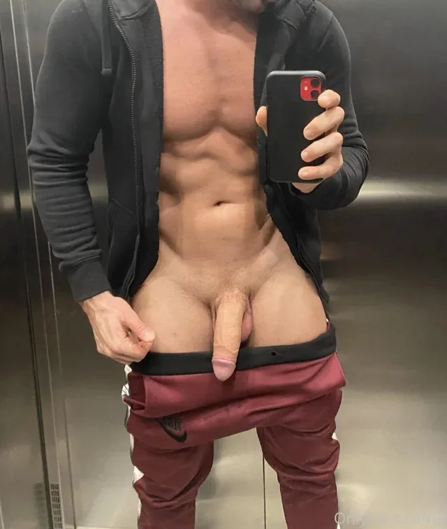 Pau duro aparecendo enquanto cara musculoso tira selfie no espelho com moletom aberto e calça abaixada
