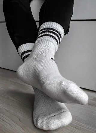 Sporty lad in striped socks teases with crossed feet on wood floor