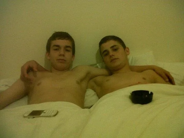 Twee scally jongens shirtless in bed, een arm gedrapeerd lui over zijn maat borst